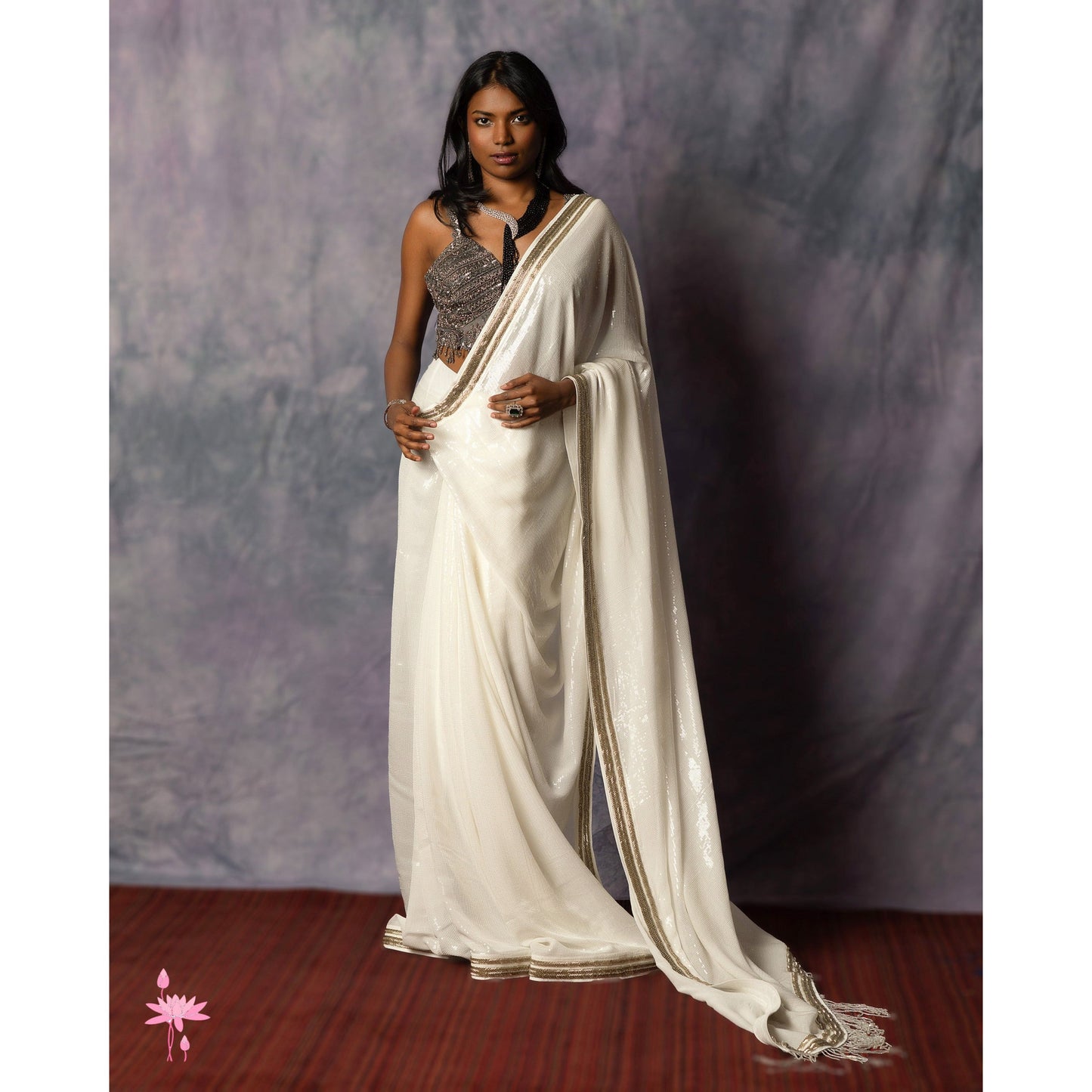 Woman wearing a white saree with a gray blouse against a plain background