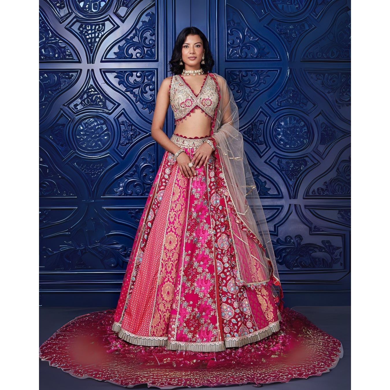 Woman in a traditional pink and red embroidered outfit against a blue decorative wall.