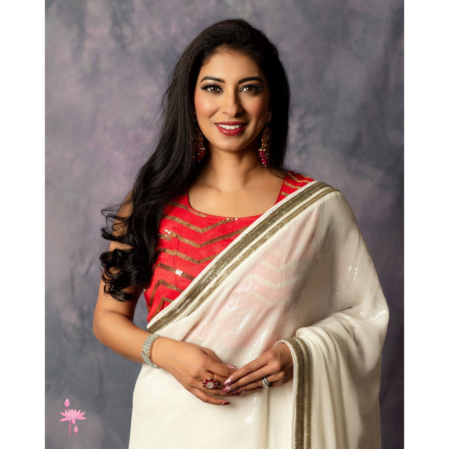 Woman wearing a red blouse and white saree with gold border against a gray background