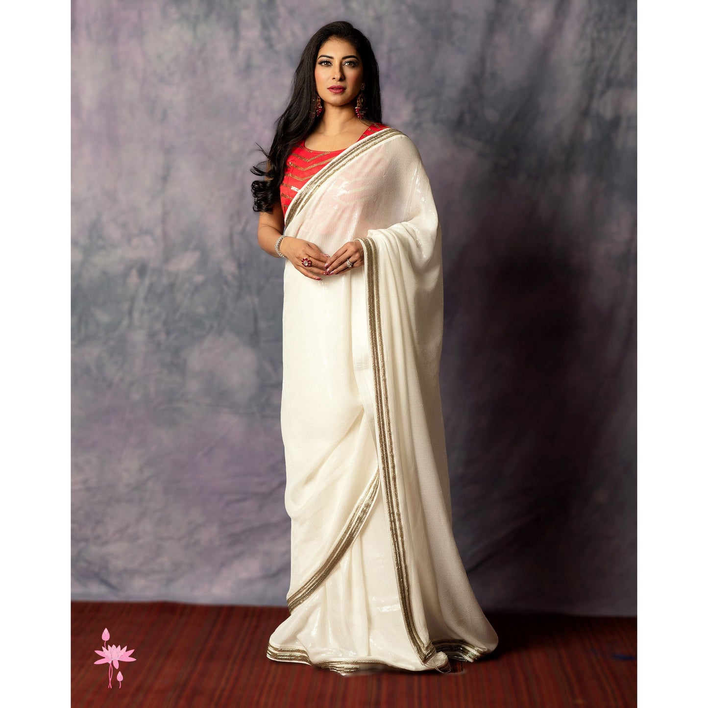 Woman wearing a white saree with a red blouse against a plain background