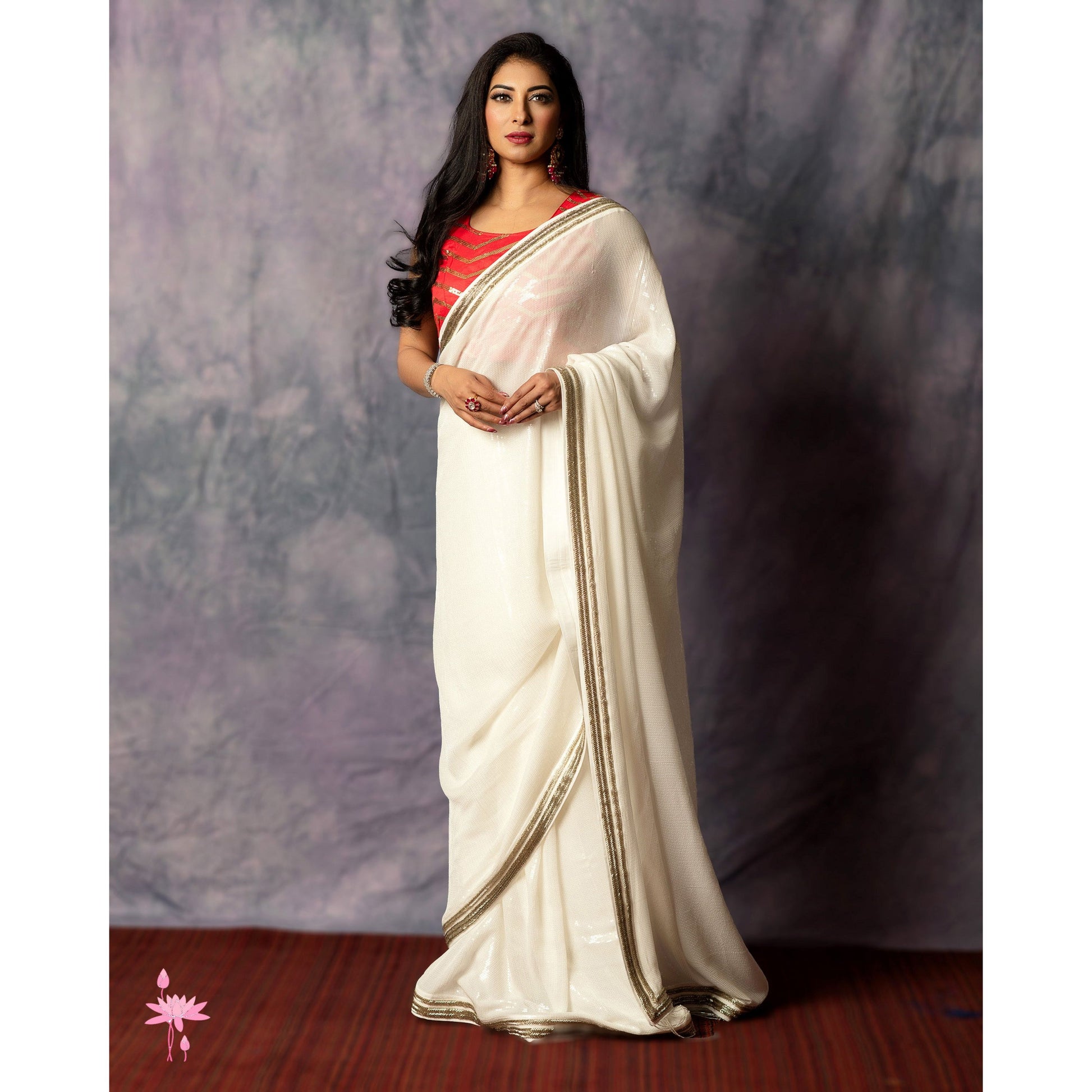 Woman wearing a white saree with a red blouse against a plain background